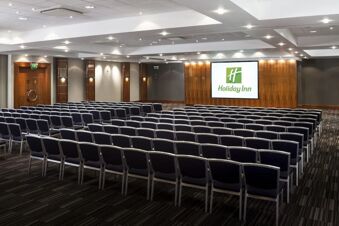 Conference room with rows of black chairs facing a screen displaying the Holiday Inn logo at Holiday Inn London-Regent's Park