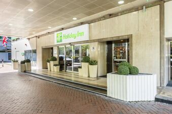 Entrance of Holiday Inn London-Regent's Park with glass automatic doors, beige planters, and trimmed green shrubs outside the building