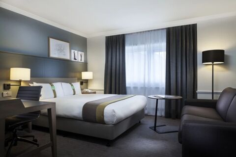 Modern hotel room at Holiday Inn London-Regent's Park with a double bed, two lamps, a desk with chair, sofa, and round table