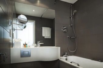 Modern hotel bathroom at Holiday Inn London-Regent's Park with white sink countertop, bathtub, mirror, and toiletries