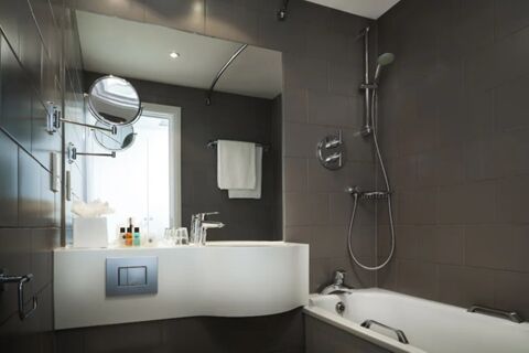 Modern hotel bathroom at Holiday Inn London-Regent's Park with white sink countertop, bathtub, mirror, and toiletries