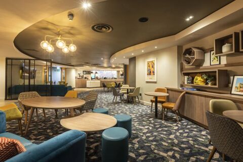 Spacious lounge area in Holiday Inn London-Regent's Park with round wooden tables and mixed chairs under warm lighting
