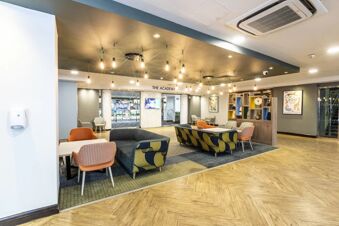 A modern seating area with patterned sofas, orange and beige chairs, hanging lights, and a glass door at Holiday Inn London-Regent's Park