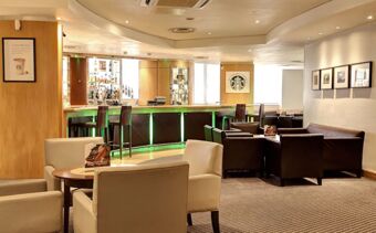 Lounge area with beige and brown chairs, round wooden tables, and a bar featuring green lights at Holiday Inn London-Regent's Park