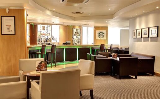 Lounge area with beige and brown chairs, round wooden tables, and a bar featuring green lights at Holiday Inn London-Regent's Park