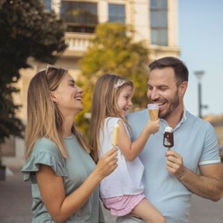 Family of three enjoying ice cream outdoors in front of Millennium Hotel London Knightsbridge building and trees