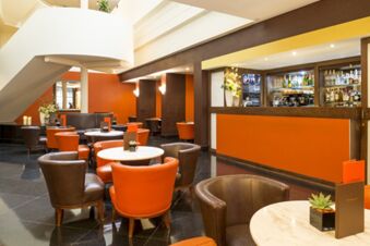Seating area with orange and brown leather chairs and white tables near a bar counter in Millennium Hotel London Knightsbridge