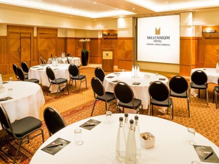 Conference room at Millennium Hotel London Knightsbridge with round tables covered in white cloths and black chairs