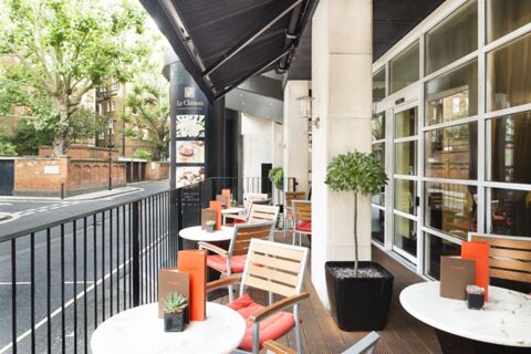 Outdoor seating area with round tables, wooden chairs with orange cushions, plants, and menus at Millennium Hotel London Knightsbridge