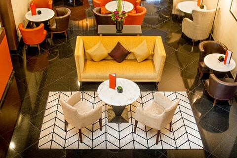 Seating area at Millennium Hotel London Knightsbridge with yellow sofa, beige and brown armchairs, white marble tables, and patterned rug
