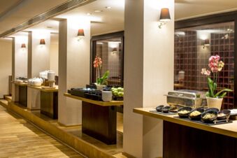 Buffet setup with chafing dishes, bowls of food, stacked plates, and pink orchids inside Millennium Hotel London Knightsbridge