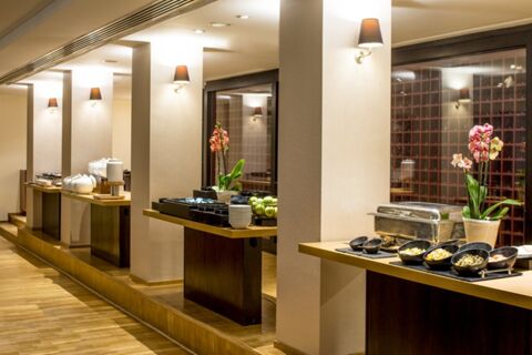Buffet setup with chafing dishes, bowls of food, stacked plates, and pink orchids inside Millennium Hotel London Knightsbridge