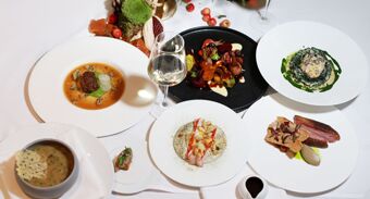 Six plated gourmet dishes and a glass of white wine on a white tablecloth with decorative autumn elements at The Lowry Hotel Manchester