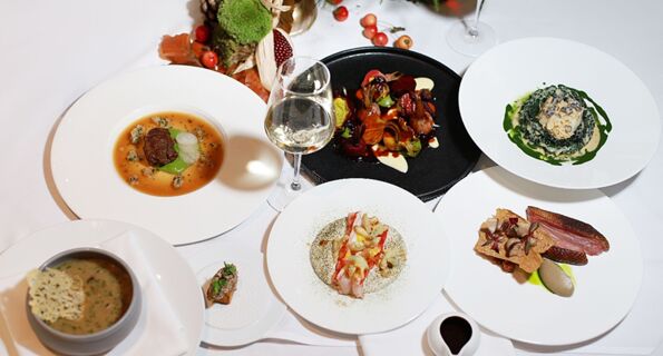 Six plated gourmet dishes and a glass of white wine on a white tablecloth with decorative autumn elements at The Lowry Hotel Manchester