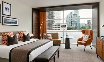 Modern hotel room at The Lowry Hotel Manchester featuring a large bed with decorative pillows and city view window