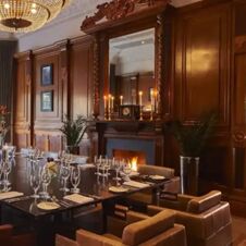 Dining table set with glassware and napkins in an elegant wood-paneled room with a chandelier fireplace and mirror at Hotel du Vin Glasgow