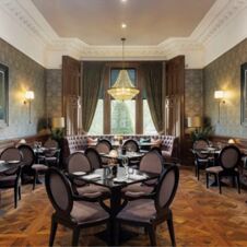Dining area at Hotel du Vin Glasgow featuring multiple round tables with chairs, a large chandelier, and patterned wallpaper