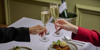 Two people clinking champagne glasses over a white tablecloth with dessert plates at Hotel du Vin Glasgow