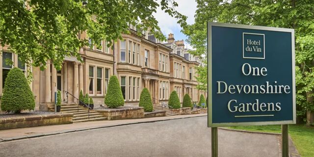 Sign for Hotel du Vin Glasgow at One Devonshire Gardens with beige stone building and neatly trimmed trees along the street