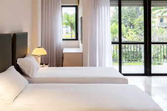 Twin white beds near a nightstand with a lamp, white curtains, window, and balcony at B&B Hotel Bari Rond&ograve;