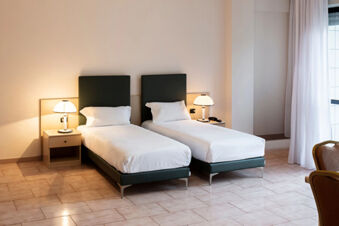 Two single beds with white linens and dark green headboards in a B&B Hotel Bari Rond&ograve; room with bedside tables and lamps