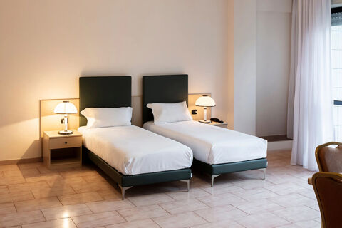 Two single beds with white linens and dark green headboards in a B&B Hotel Bari Rond&ograve; room with bedside tables and lamps
