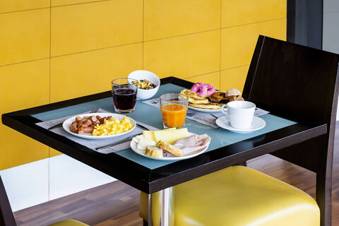 Breakfast setting with plates of scrambled eggs, sausages, cheese, sliced ham, juice, coffee, and pastries on a table at B&B Hotel Bari Rond&ograve;