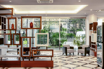 Lobby area at B&B Hotel Bari Rond&ograve; with wooden open shelving, two armchairs, large windows, and patterned floor tiles