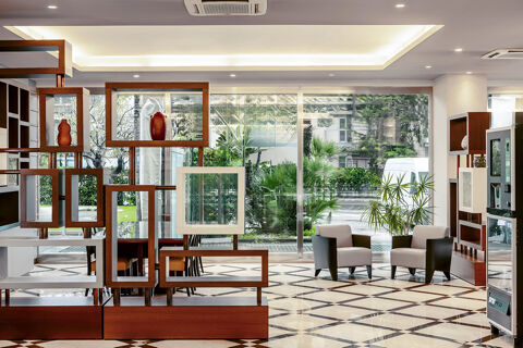 Lobby area at B&B Hotel Bari Rond&ograve; with wooden open shelving, two armchairs, large windows, and patterned floor tiles