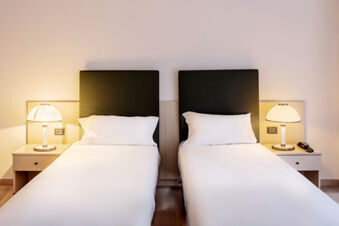Two single beds with black headboards, white bedding, and bedside tables with lamps at B&B Hotel Bari Rond&ograve;