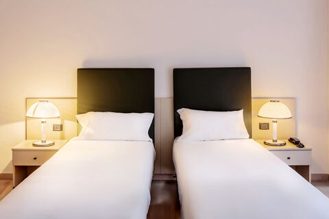 Two single beds with black headboards, white bedding, and bedside tables with lamps at B&B Hotel Bari Rond&ograve;