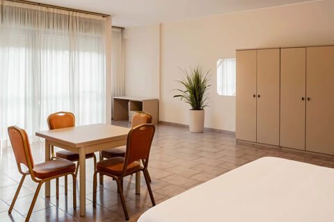 A spacious room at B&B Hotel Bari Rond&ograve; with a dining table and four chairs near sheer curtains and a large cabinet