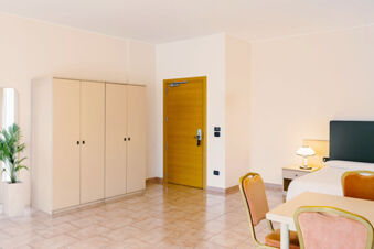 Hotel room at B&B Hotel Bari Rond&ograve; with beige wardrobe, wooden door, white bed, nightstand with lamp, and pink chairs around table