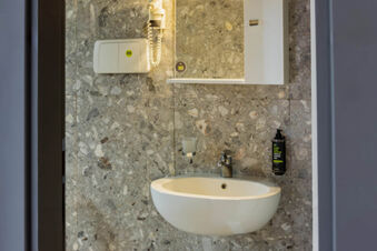 Bathroom sink with a faucet, wall-mounted soap dispenser and cup holder, a hairdryer, and a mirror in B&B Hotel Bari Rond&ograve;