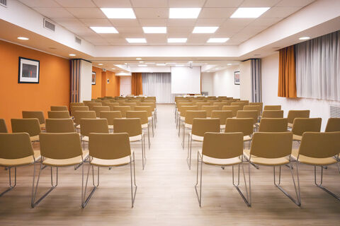 Rows of beige chairs facing a projector screen in a conference room at B&B Hotel Bari Rond&ograve; with orange and white walls