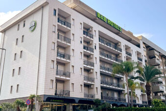 Modern multi-story building with balconies, air conditioning units, palm trees, and B&B Hotel Bari Rond&ograve; signage on the facade