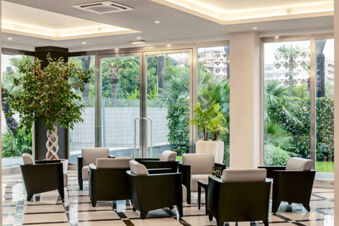 Lounge area at B&B Hotel Bari Rond&ograve; with black and white armchairs surrounding small tables near large glass windows and green plants