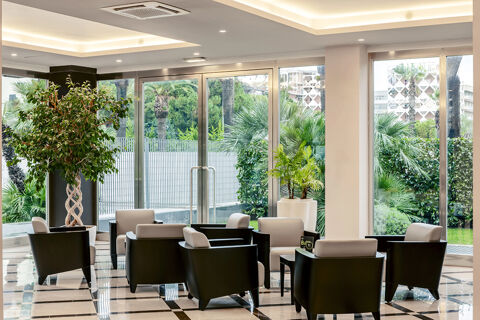 Lounge area at B&B Hotel Bari Rond&ograve; with black and white armchairs surrounding small tables near large glass windows and green plants
