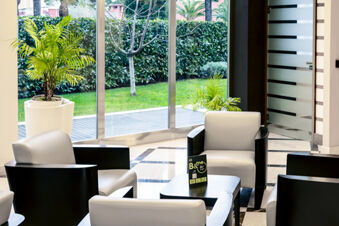 Modern seating area with beige and black armchairs around a black table and plants near large windows at B&B Hotel Bari Rond&ograve;