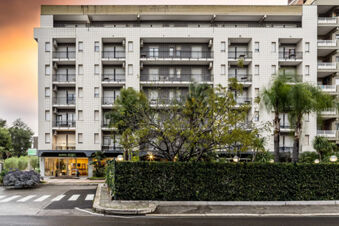 Multi-story building with balconies, palm trees, and greenery in front showing the entrance of B&B Hotel Bari Rond&ograve;