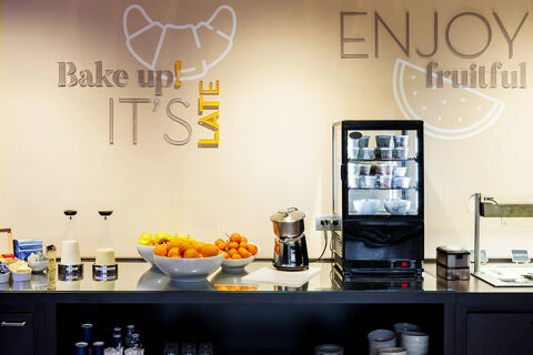 Breakfast counter with fruit bowls, milk pitchers, a small fridge, and wall art at B&B Hotel Bari Rond&ograve;