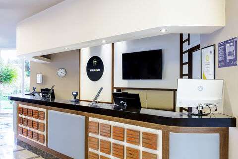 Reception desk area with black countertop, computer monitors, a wall clock, and B&B Hotel Bari Rond&ograve; welcome sign visible