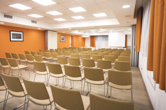 Conference room with rows of beige chairs facing a white projector screen and orange walls at B&B Hotel Bari Rond&ograve;