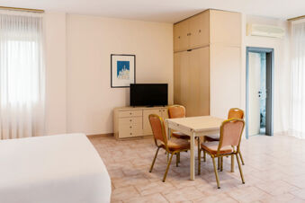 Bright hotel room at B&B Hotel Bari Rond&ograve; with bed, four chairs around a table, TV on a dresser, and built-in closet