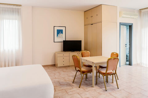 Bright hotel room at B&B Hotel Bari Rond&ograve; with bed, four chairs around a table, TV on a dresser, and built-in closet