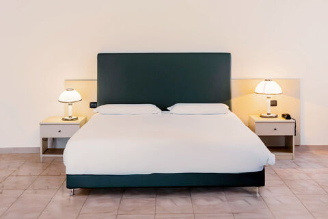 Double bed with black headboard, white bedding, two pillows, and bedside tables with lamps in B&B Hotel Bari Rond&ograve;
