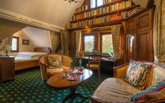 A cozy room at Burghotel Auf Sch&ouml;nburg with antique wooden furniture, bookshelves, patterned cushions, and a bed visible through the archway
