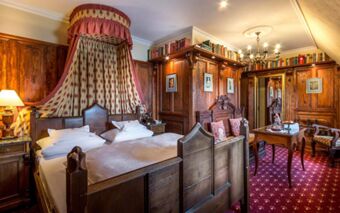 Bedroom at Burghotel Auf Sch&ouml;nburg with wooden furniture, a canopy bed, red carpet, chandelier, and books on shelves