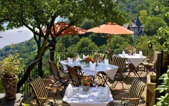 Outdoor dining area at Burghotel Auf Sch&ouml;nburg with striped chairs, white tablecloths, orange umbrellas, and river views