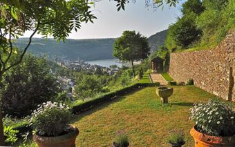 Garden area with flower pots, a stone wall, trees, and a river view overlooking a town near Burghotel Auf Sch&ouml;nburg